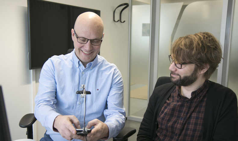 Tutkimusjohtaja Raino Vastamäki testaa kännykällä palvelun saavutettavuutta. Kännykässä on kiinni kamera, jolla voi kuvata palvelun käyttöä. Vieressä saavutettavuusasiantuntija Timo Övermark.