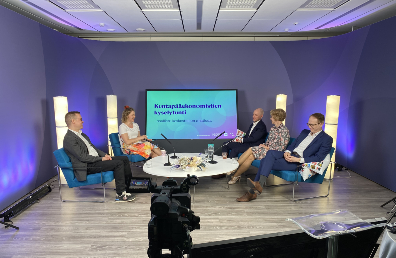 Miehiä ja naisia istumassa tv-studiossa penkeillä.