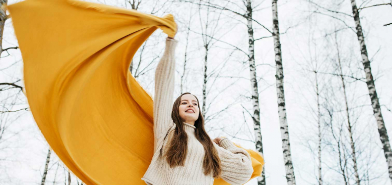 Nainen pitelee käsien yläpuolella keltaista huivia ja hymyilee.