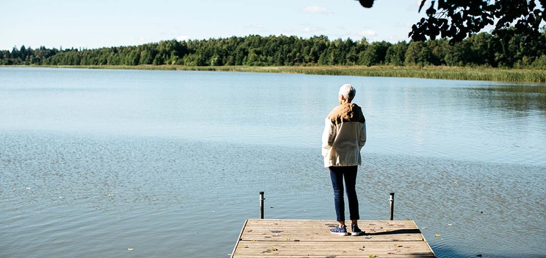 Nainen on selin kameraan laiturilla ja katselee kaukaisuuteen.